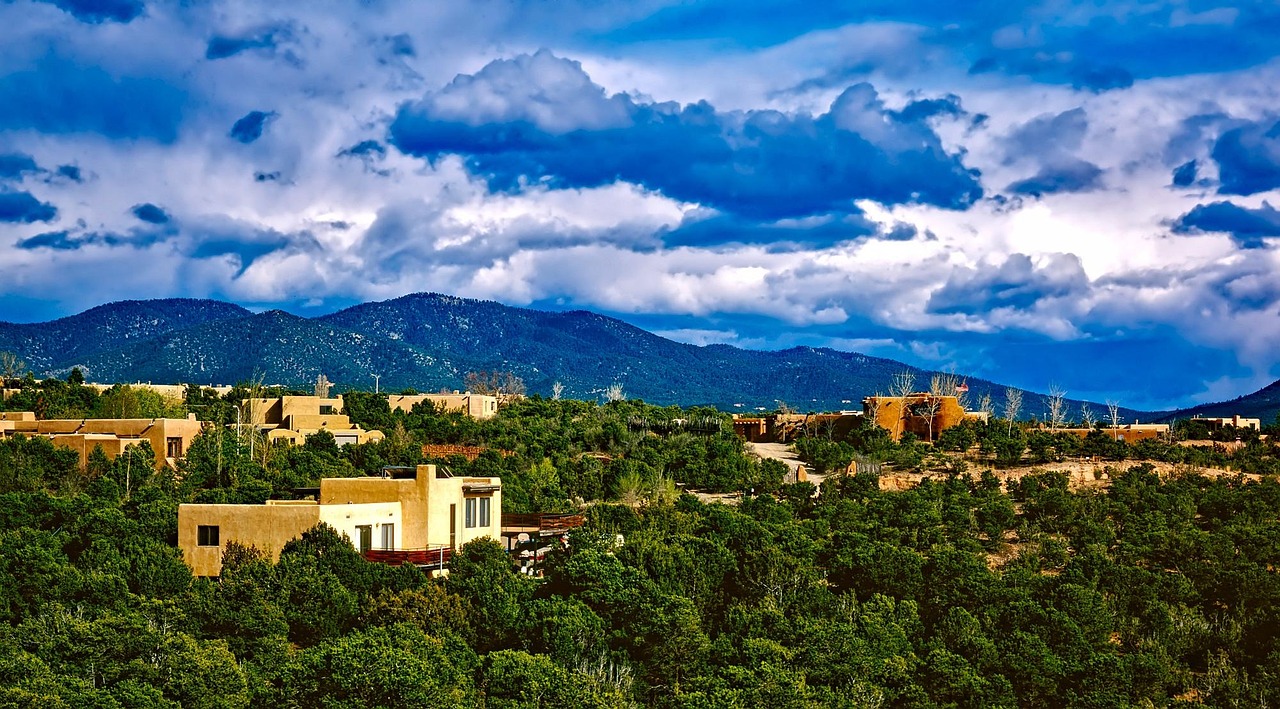 Earthy adobe walls, vivid turquoise doors, and desert blooms — the warm, artistic heart of must-visit places in the USA Adobe-style buildings with turquoise doors and blooming purple flowers in Santa Fe plaza
