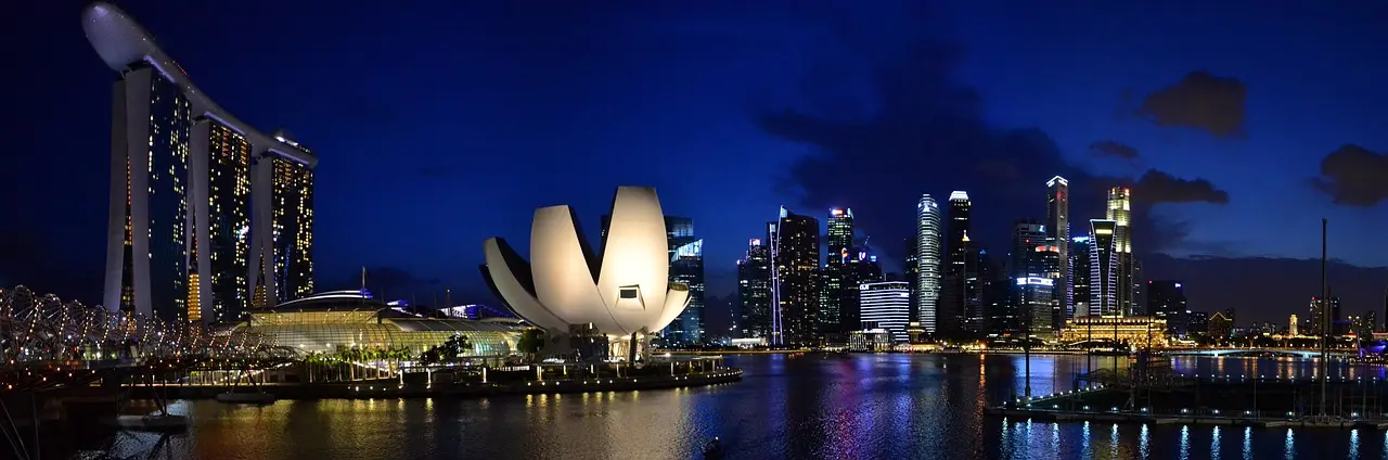 Aerial view of Singapore’s Marina Bay skyline at dusk with illuminated skyscrapers and waterfront promenade