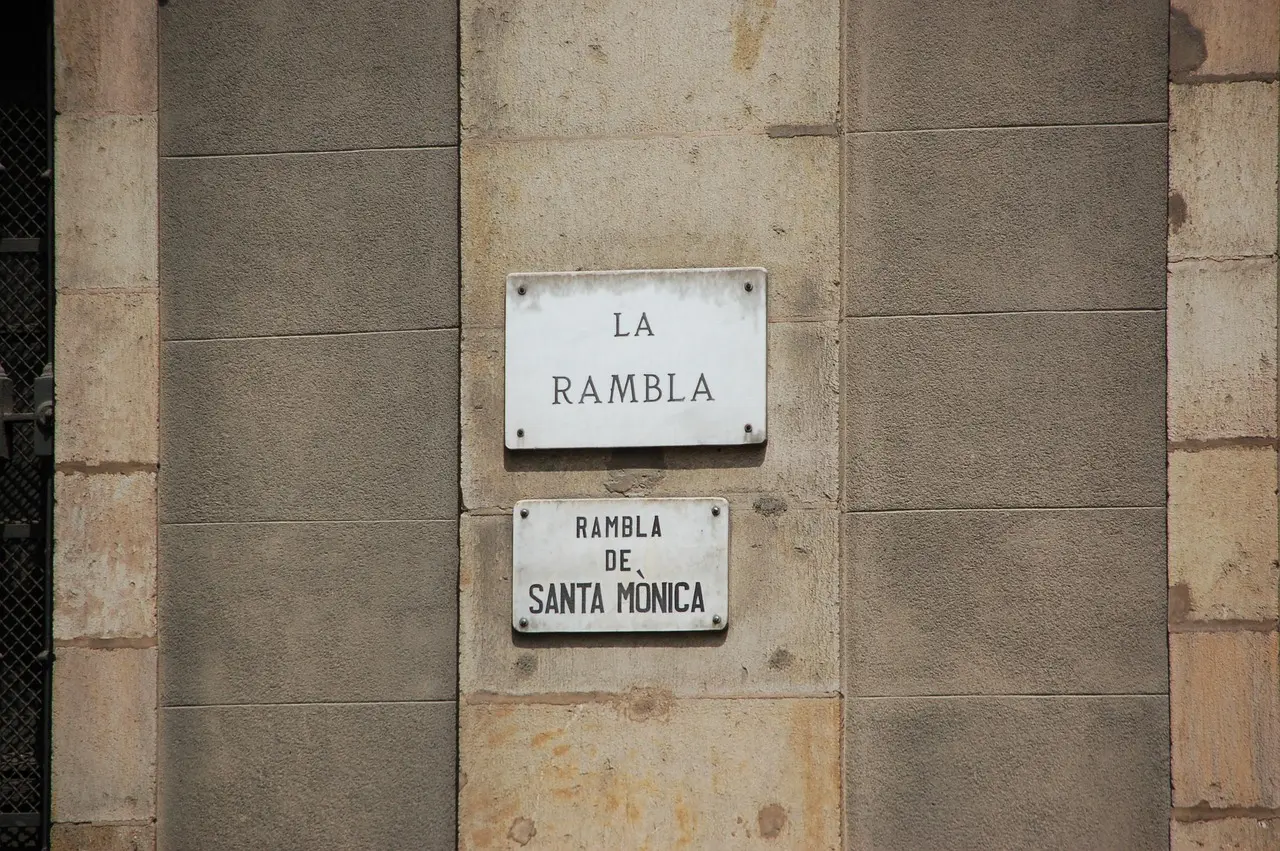 The vibrant energy of La Rambla in Barcelona — a sensory-rich artery linking history, commerce, and performance among must-visit places in Spain. Crowded La Rambla street with striped awnings, street performers, and palm trees