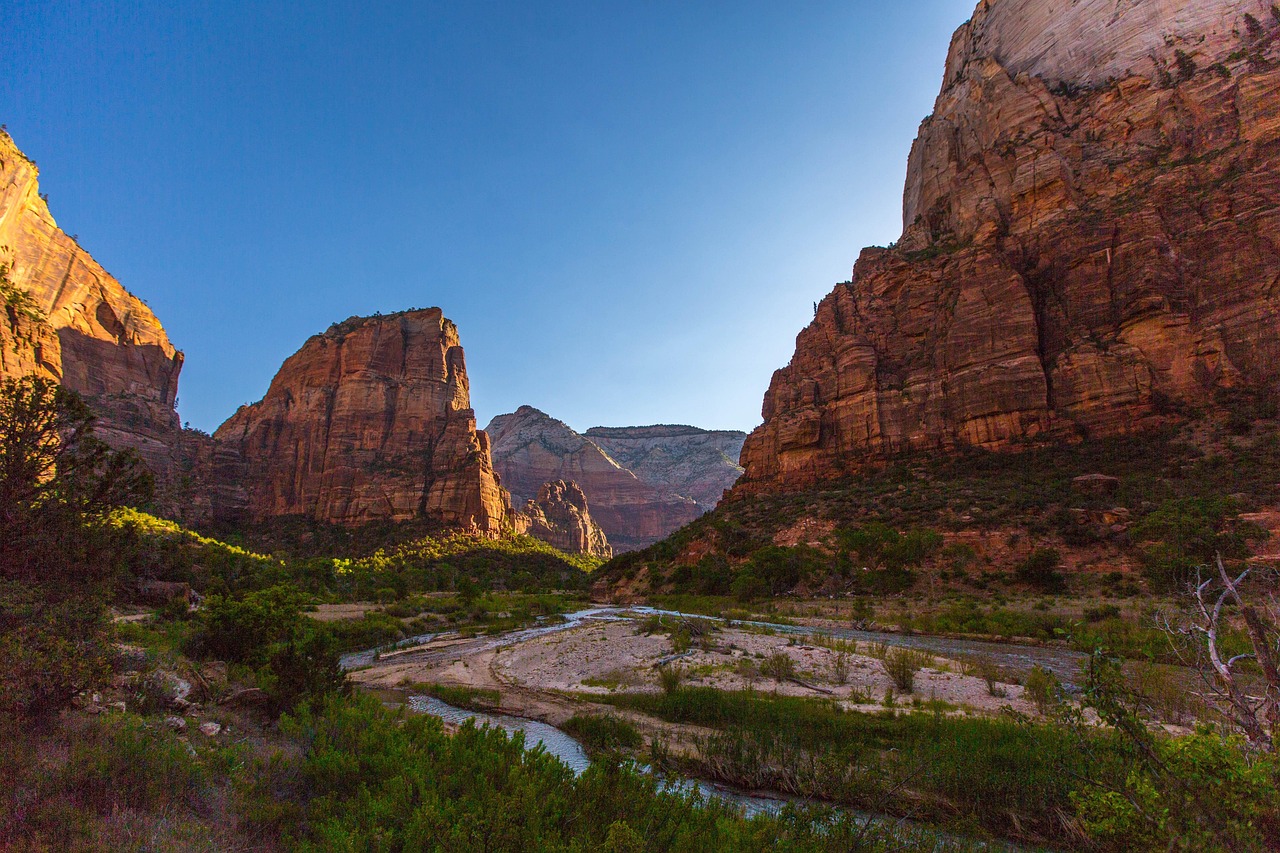 Sunlit sandstone walls soar above a winding desert trail — a breathtaking scene among must-visit places in the USA Towering red sandstone cliffs flanking narrow canyon with hikers on trail