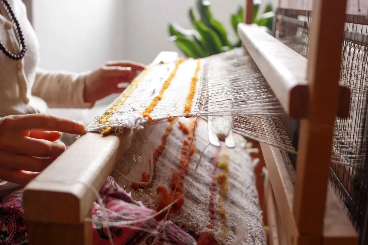 Authentic Zapotec weaving workshop in Teotitlán del Valle, Oaxaca—preserving pre-Hispanic textile techniques Indigenous Zapotec woman smiling as she demonstrates backstrap loom weaving with vibrant wool threads in a sunlit adobe workshop
