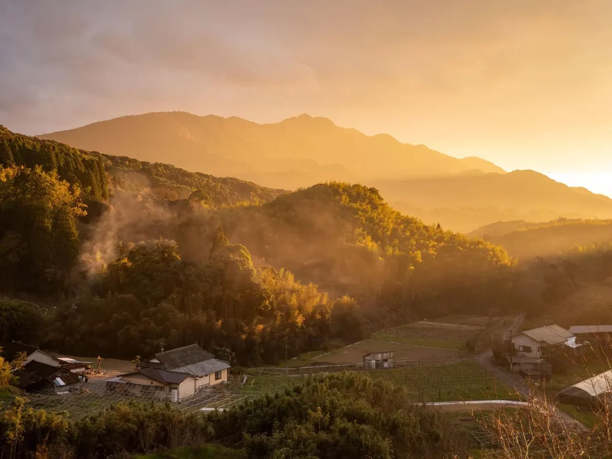 A person sitting peacefully on a wooden deck overlooking misty mountains at dawn, eyes closed, breathing deeply