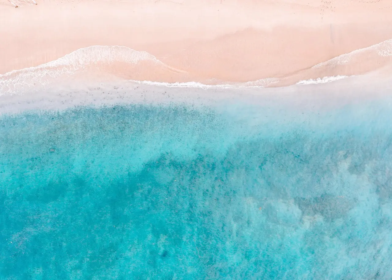Serene coastal cove at dawn — an ideal 2026 travel destination for relaxation on untouched shores Aerial view of a quiet coastal cove with turquoise water, white sand, and lush green cliffs at sunrise