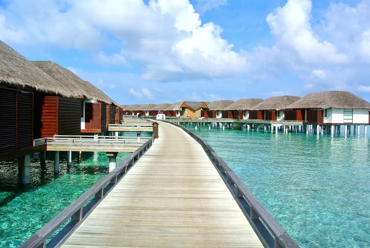 Aerial view of turquoise waters lapping against white-sand beach with palm trees and a secluded overwater bungalow