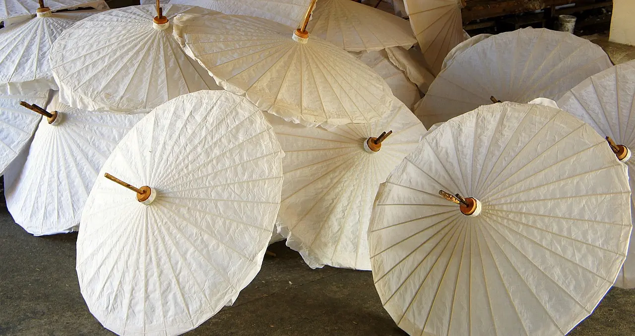 Traditional Lanna paper umbrella painting workshop in Chiang Mai’s Bo Sang village Thai artisan painting delicate floral patterns on a hand-stretched paper umbrella in a Chiang Mai village workshop