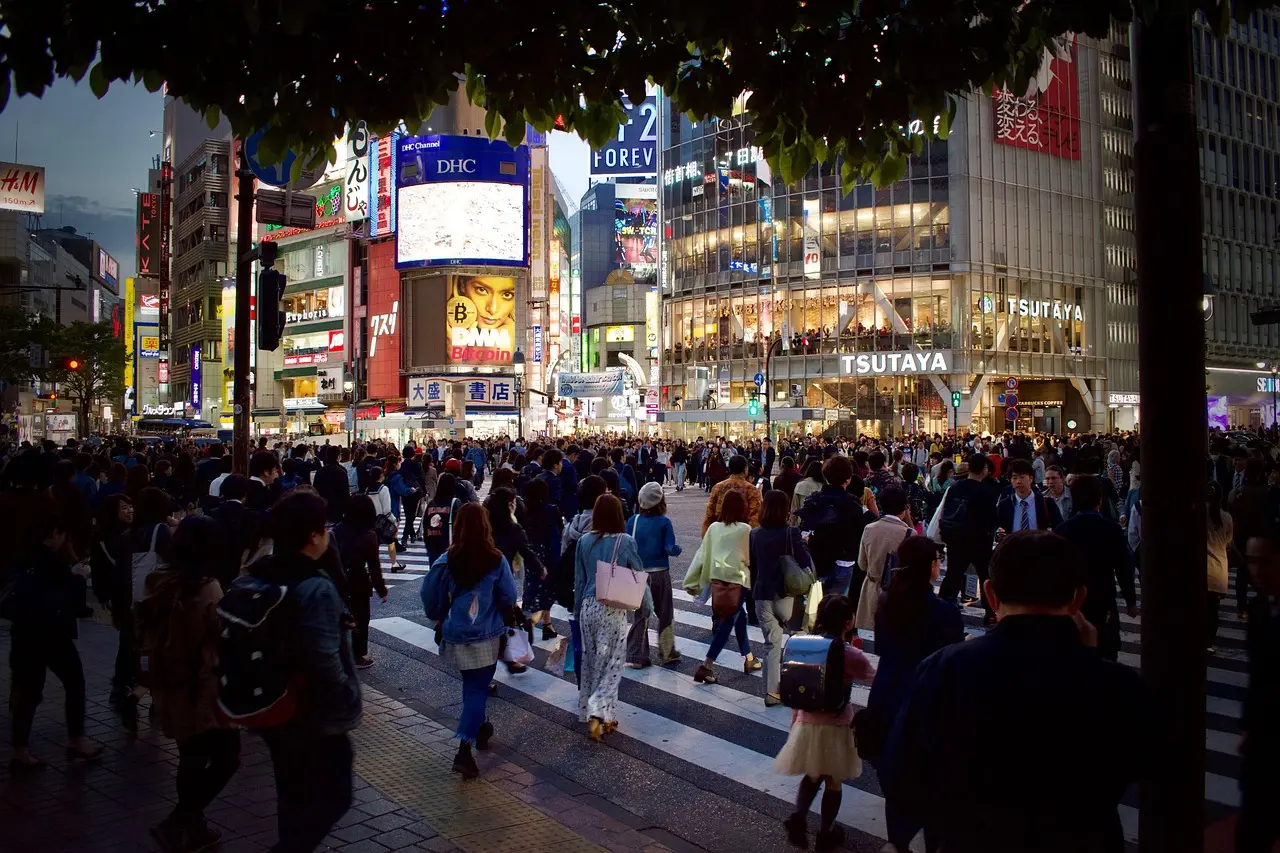 Aerial view of Tokyo's Shibuya Crossing at dusk, filled with pedestrians and neon signs