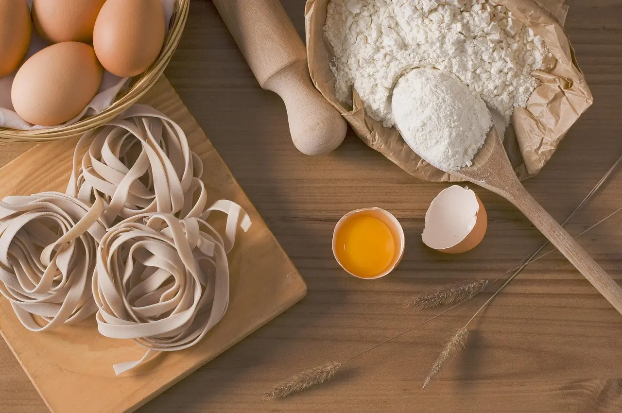 Authentic pasta-making workshop in Bologna where participants learn traditional tagliatelle technique from a third-generation chef Hand-rolling fresh egg pasta on a wooden board in a sunlit Bolognese kitchen