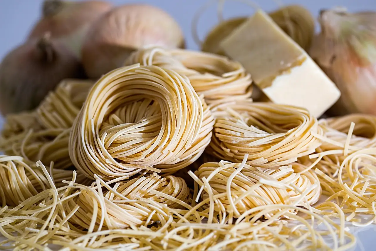 Traditional handmade pasta workshop in Lucca, Italy—using heritage recipes and time-honored tools Close-up of hands rolling fresh pasta dough with a wooden rolling pin on a floured marble surface in a rustic Tuscan kitchen