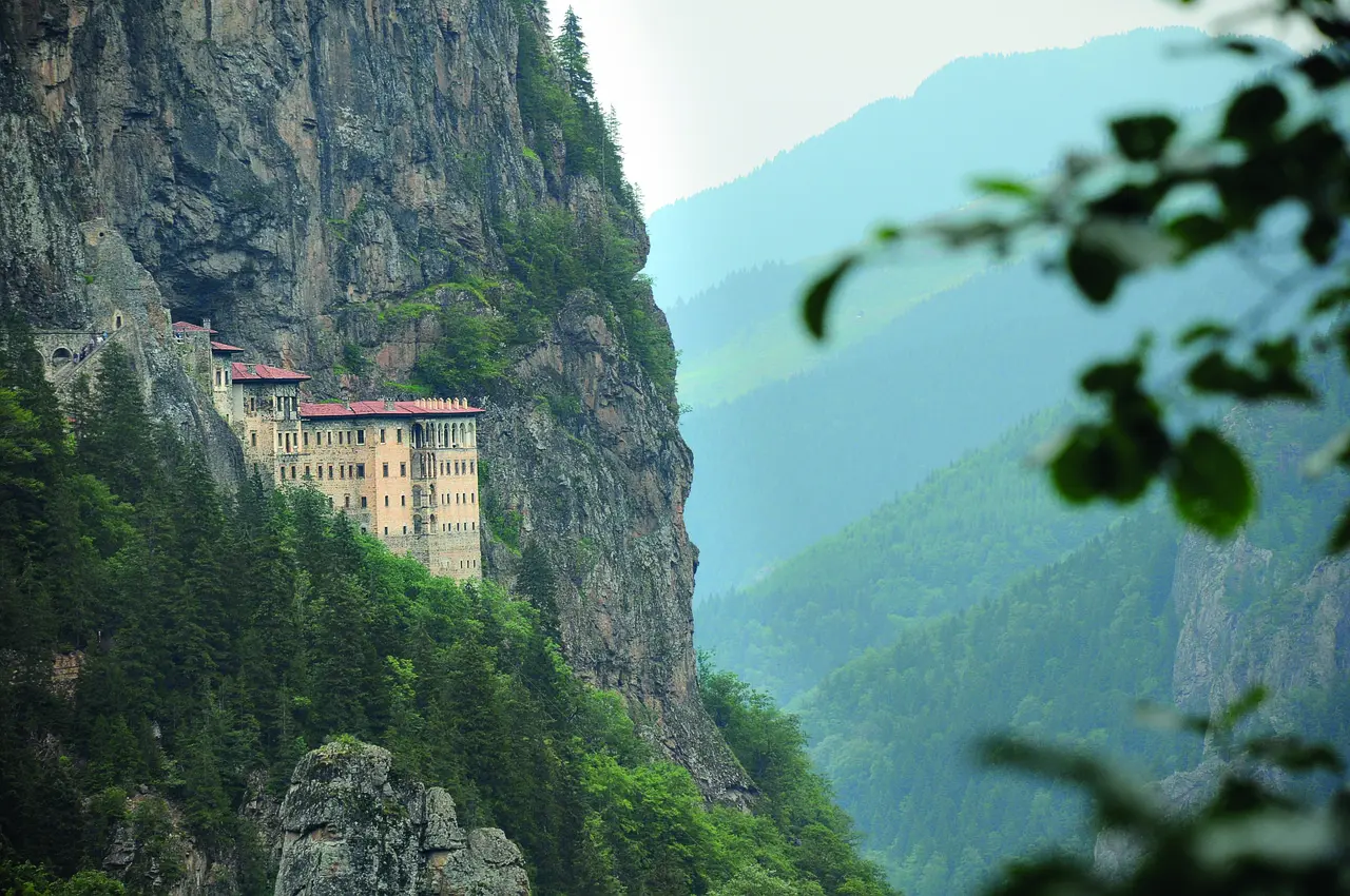 Sumela Monastery embedded in a green cliff face with clouds drifting by