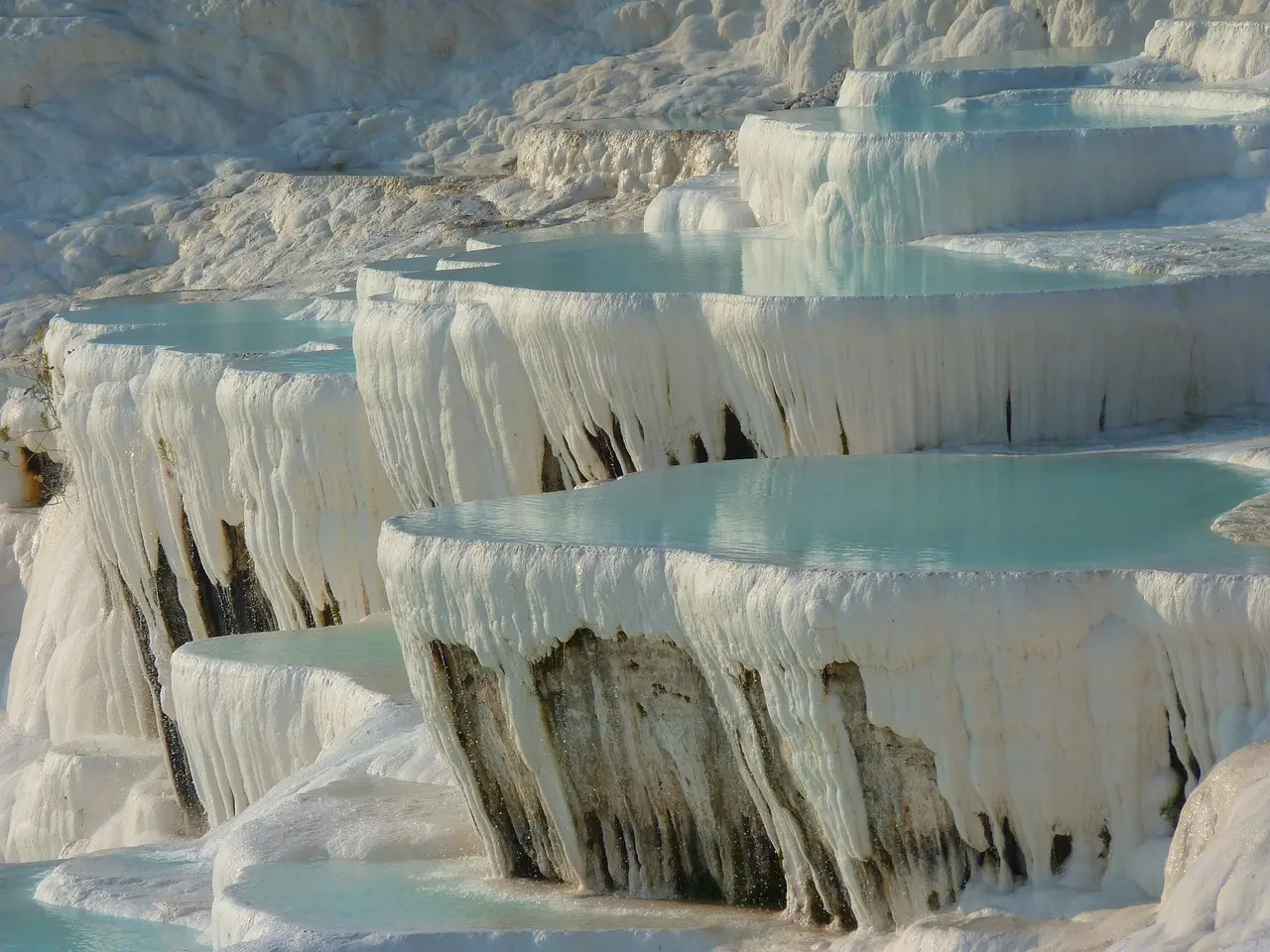 Travertine terraces of Pamukkale filled with turquoise water under clear sky